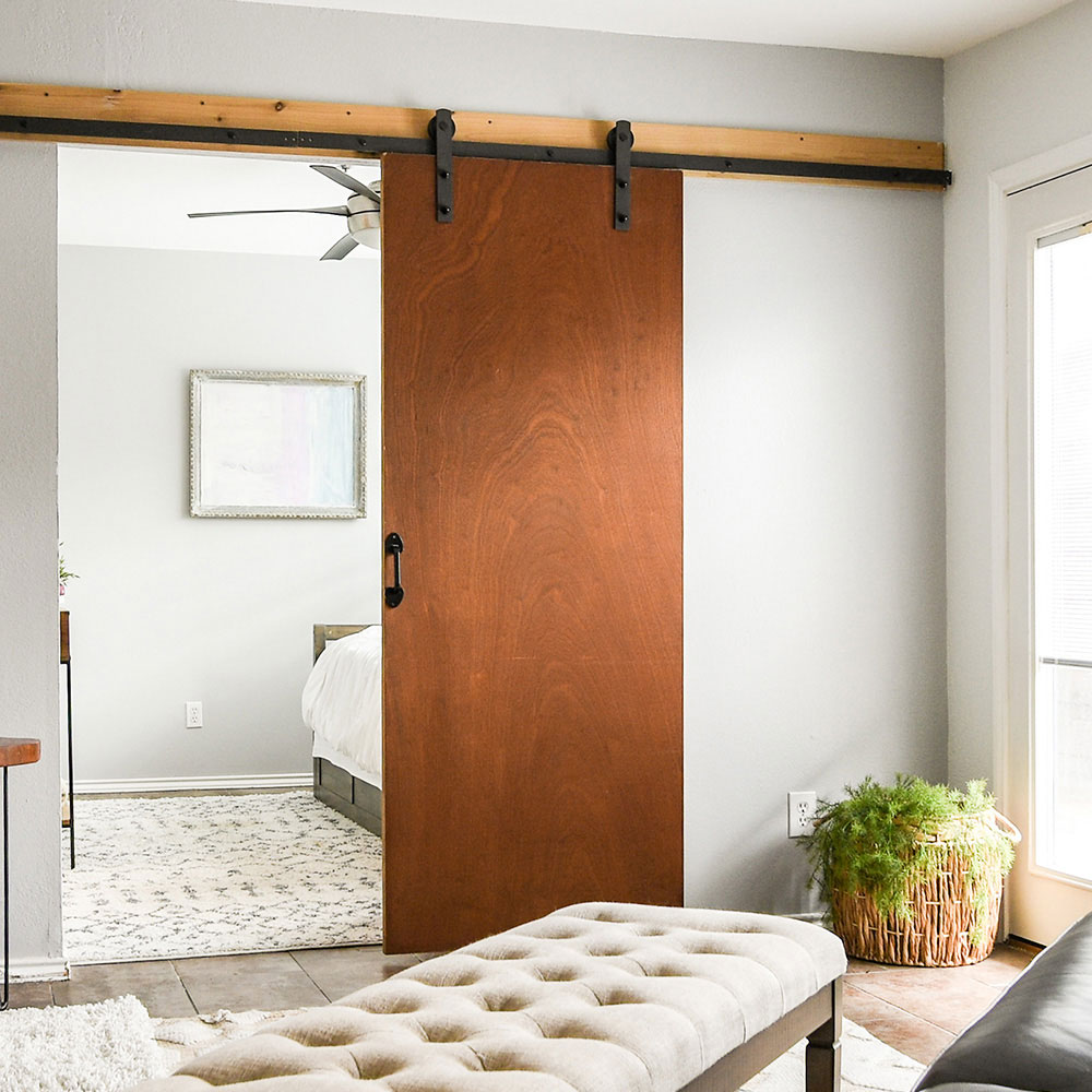 Flat wood-grain barn door on black hardware partially covering a bedroom entry