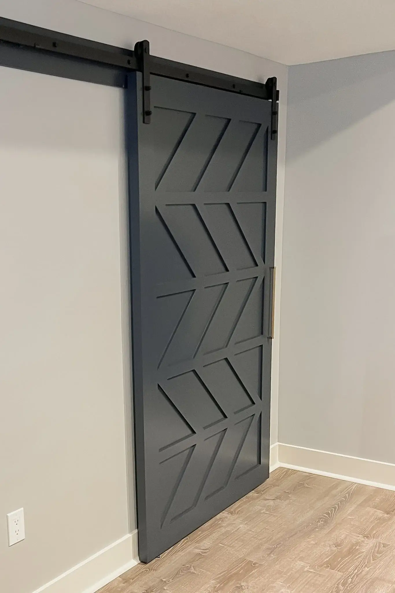 Dark gray chevron barn door mounted on a black track against a light wall