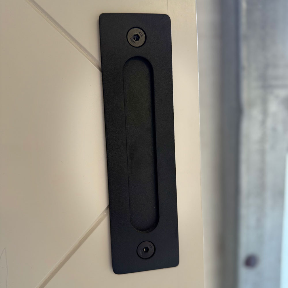 Black rectangular recessed pull mounted flush into a white barn door