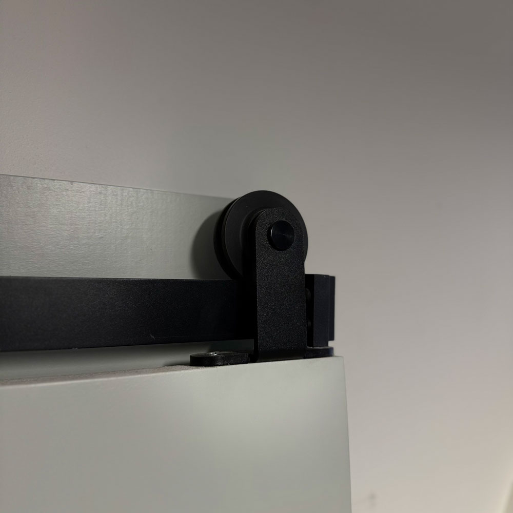 Close detail of a black barn-door wheel hanger riding on a flat steel rail