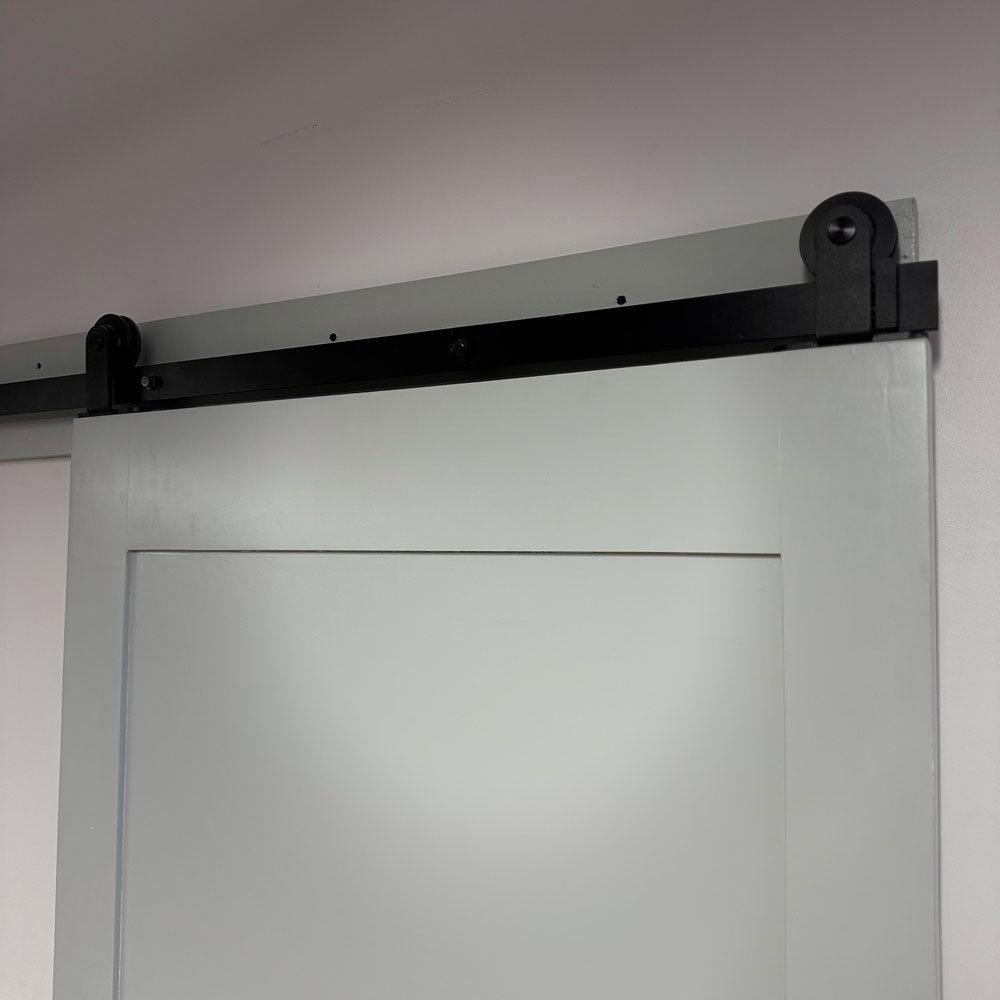Black steel barn-door rail and wheel hangers installed above a white sliding door