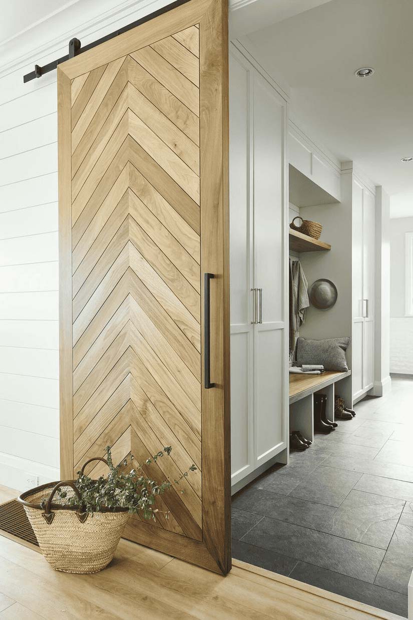 Light wood chevron barn door on a black track in a mudroom