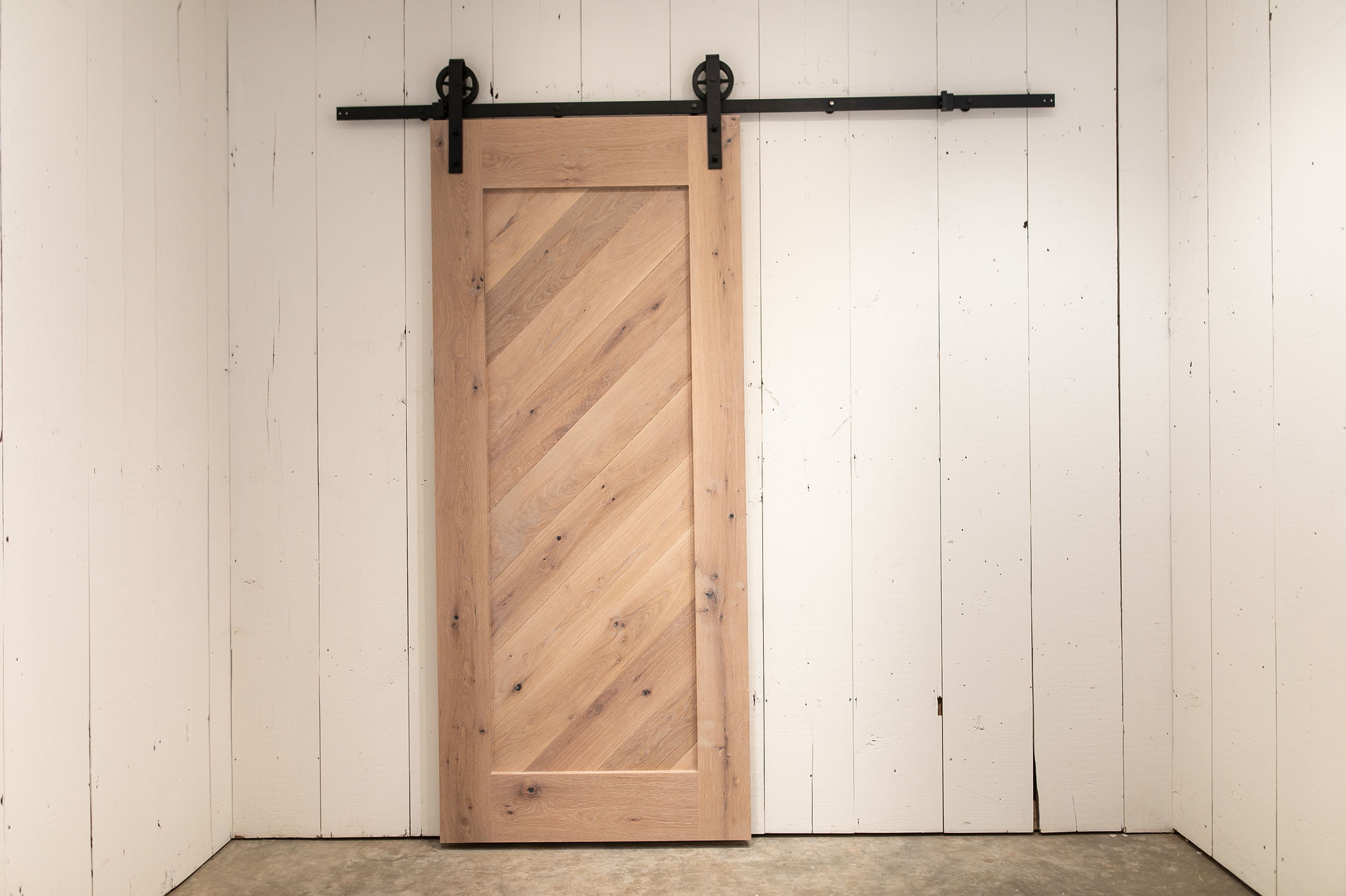 Light wood sliding barn door with diagonal planks against a white paneled wall