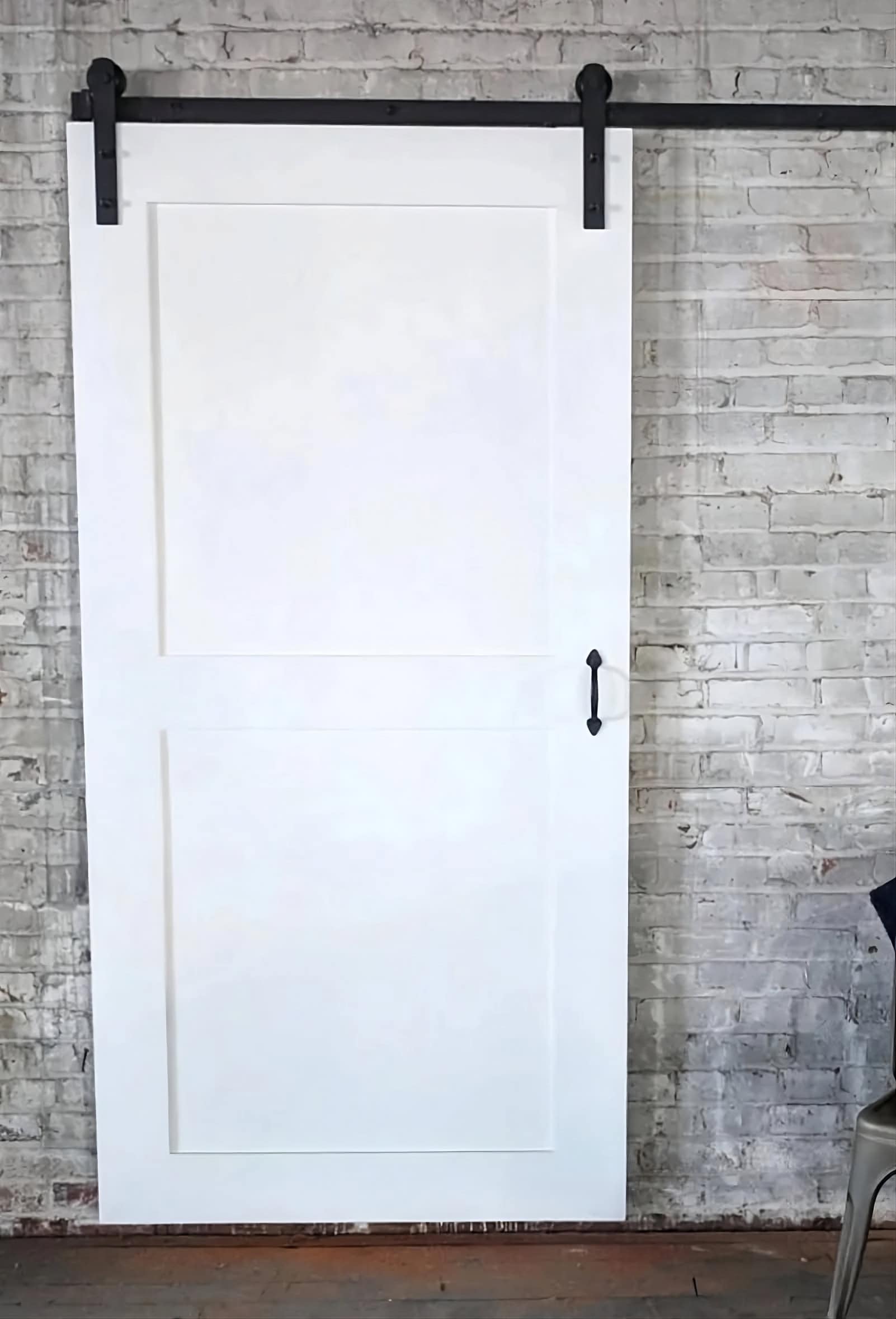 White two-panel sliding barn door on black hardware against a white brick wall