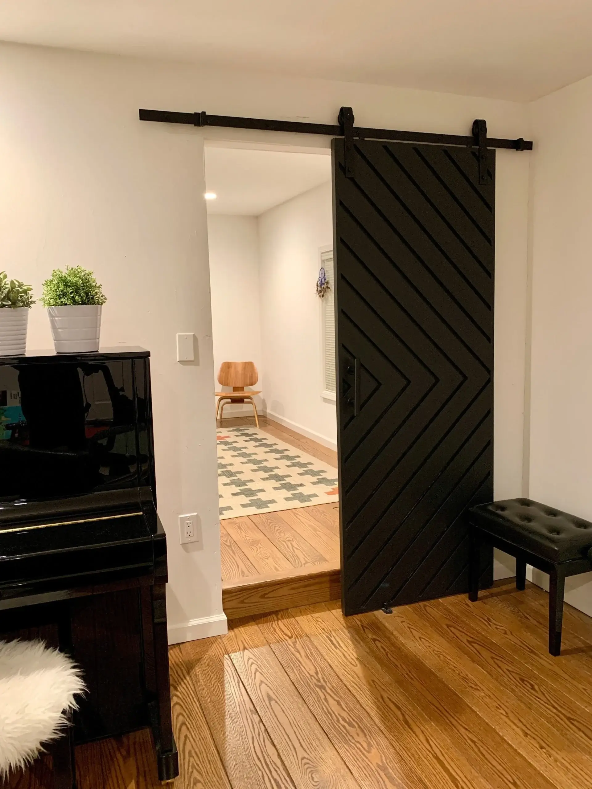 Black chevron-pattern barn door installed beside a piano