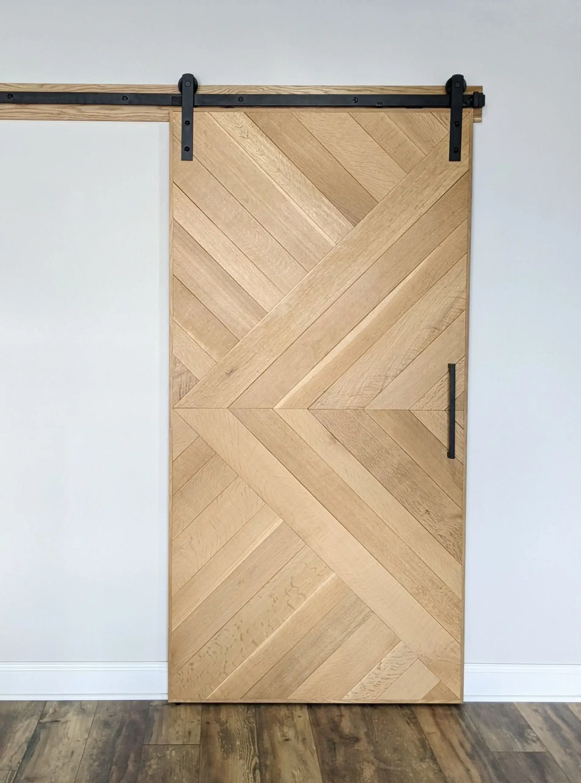 Light wood barn door with a geometric chevron pattern on black hardware