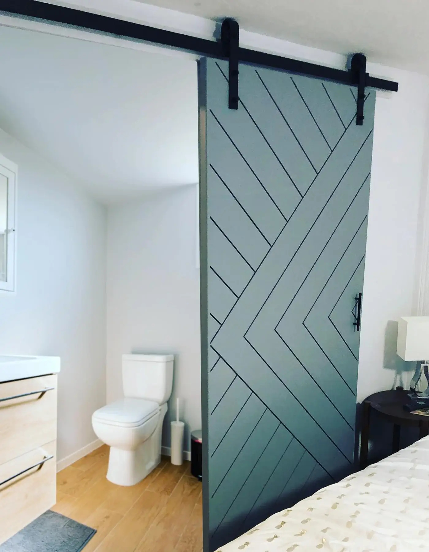 Gray geometric chevron barn door separating a bedroom and bathroom