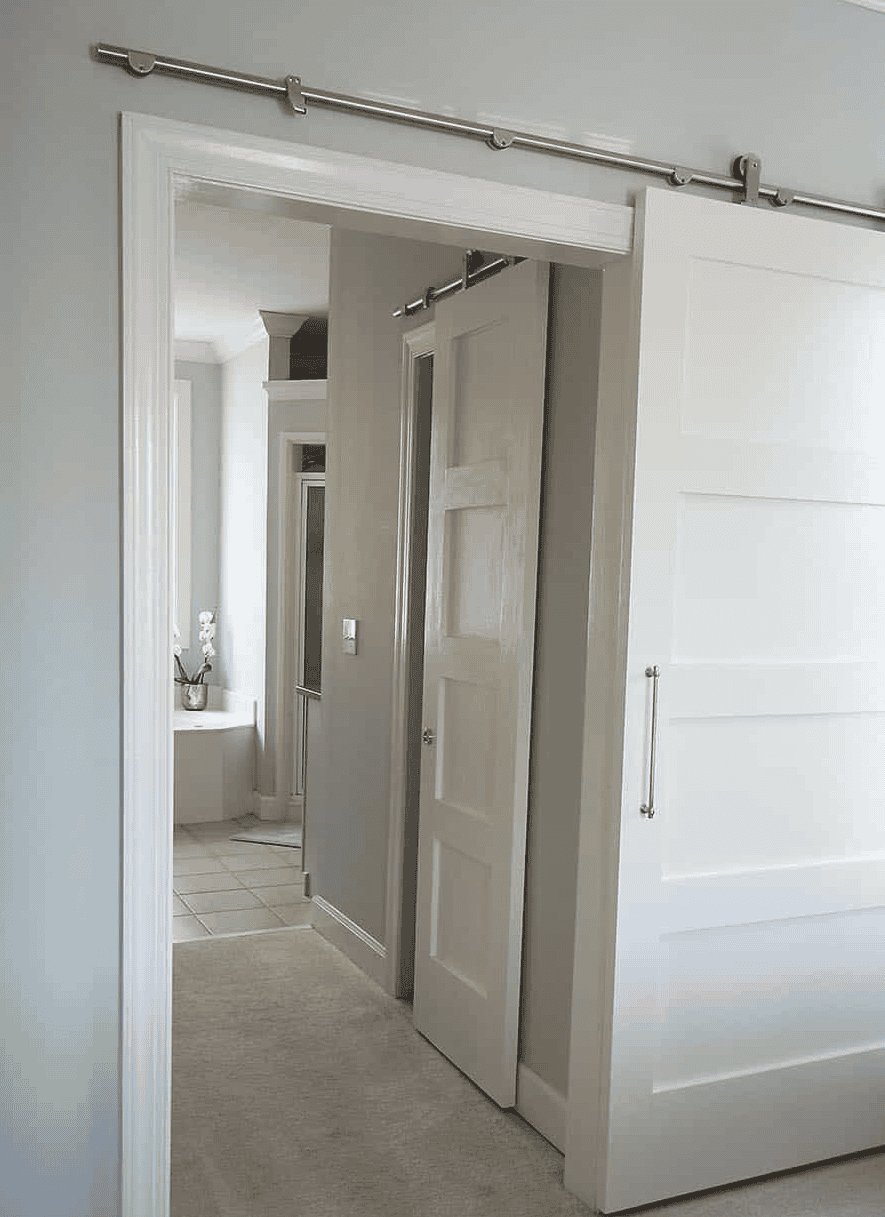 White four-panel sliding barn door partially open to a hallway and bathroom