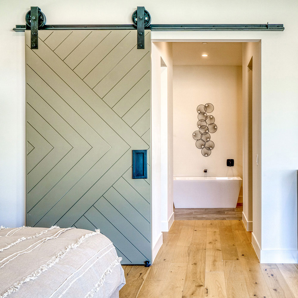 Muted green barn door with intersecting diagonal geometric lines opening to a bathroom