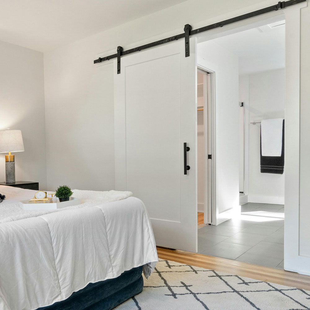 Solid white sliding barn door with black hardware between a bedroom and bathroom