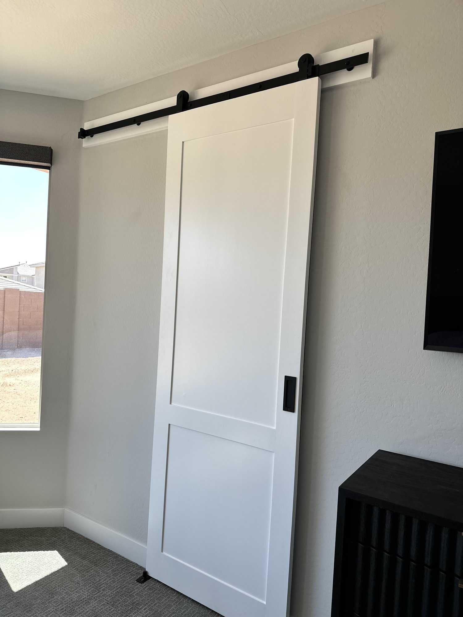 White two-panel sliding barn door installed beside a window on a light gray wall