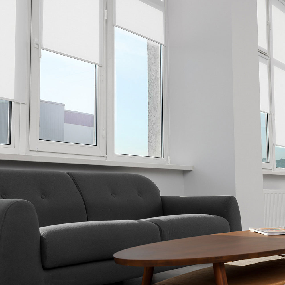 White roller shades behind a gray sofa in a living room
