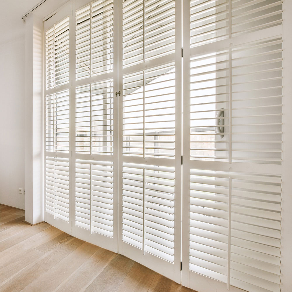 White plantation shutters mounted over a full-height glass door