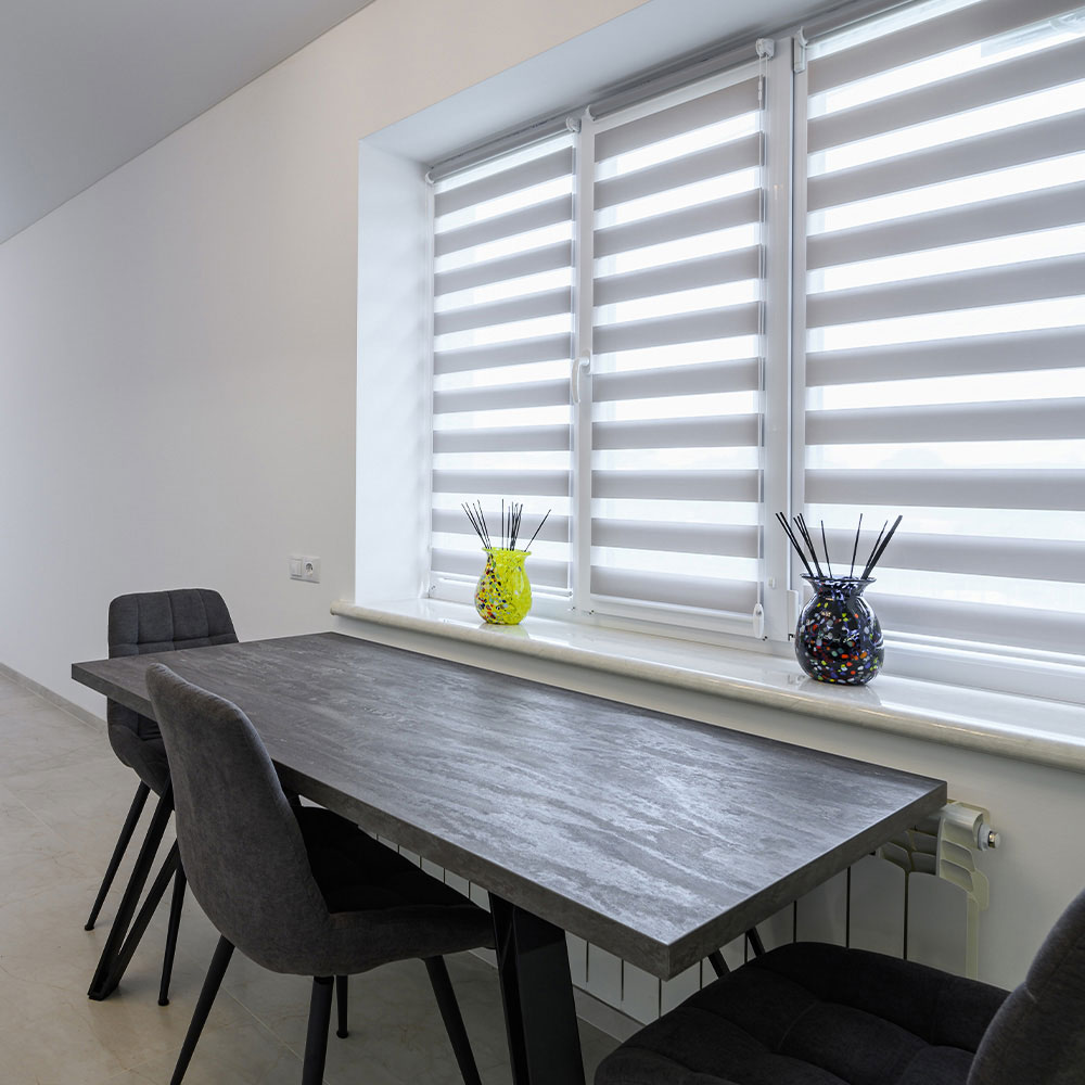 White zebra shades filtering light beside a dining table
